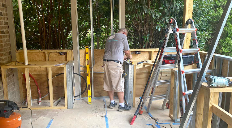 A man works on framing a wall in a construction area, tools and a ladder nearby.