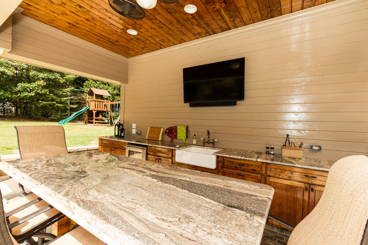 An outdoor kitchen with granite counter tops and a tv.