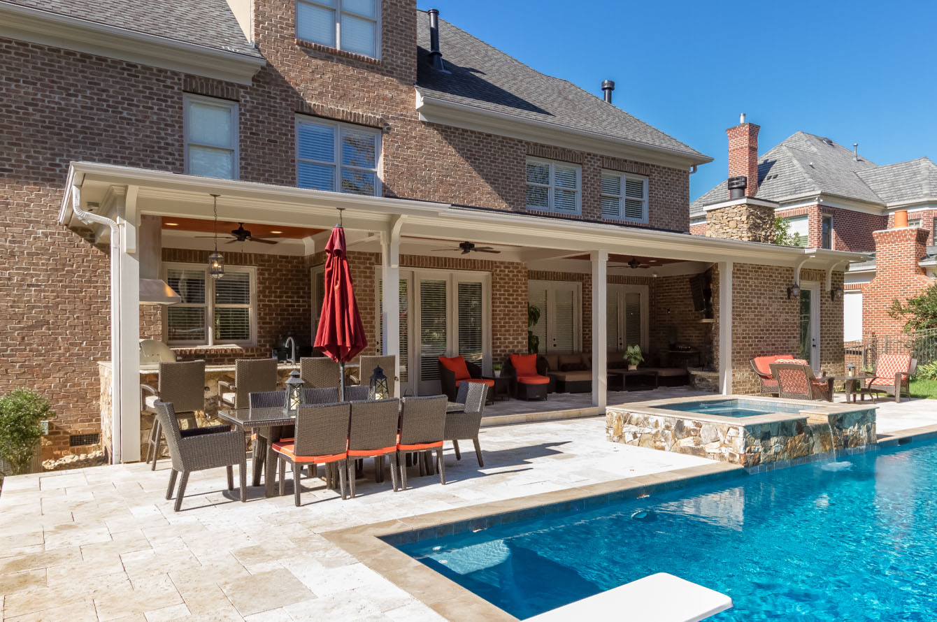 Elegant backyard featuring outdoor living amenities such as a pool, covered patio, furnished dining and lounge areas, and a brick house with large windows.