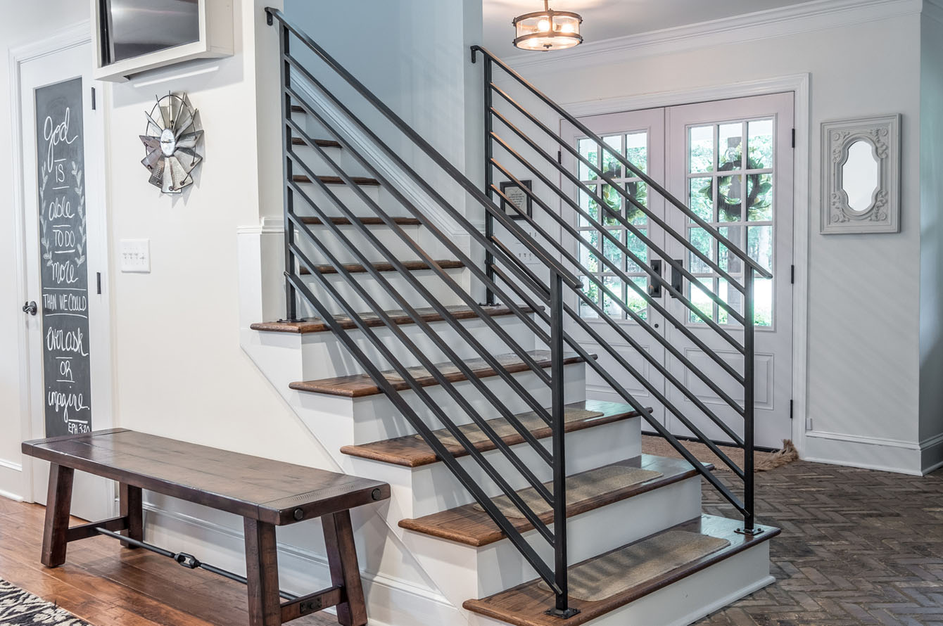 A modern staircase with wooden steps and black metal railings in a well-lit entryway featuring decorative elements and a bench, perfectly complements the new home addition.