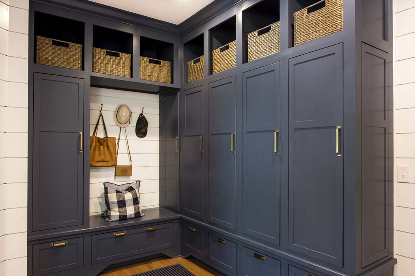 A stylish home addition with navy cabinets, built-in seating, and wicker storage baskets, highlighted by brass handles and a white paneled wall.