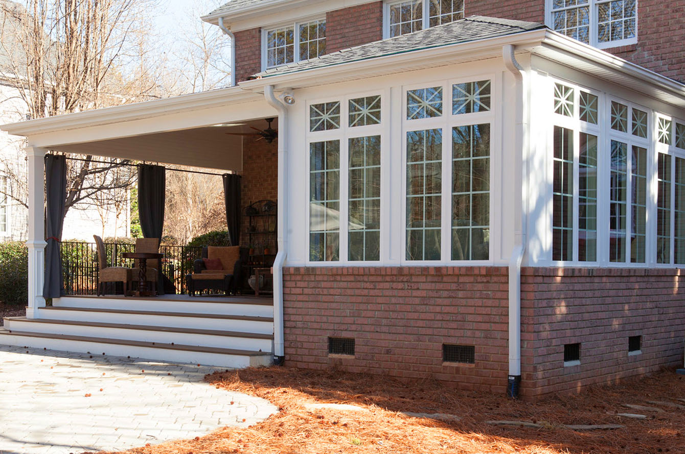 Exterior of a brick house with a sunroom home addition and an attached covered porch featuring patio furniture.