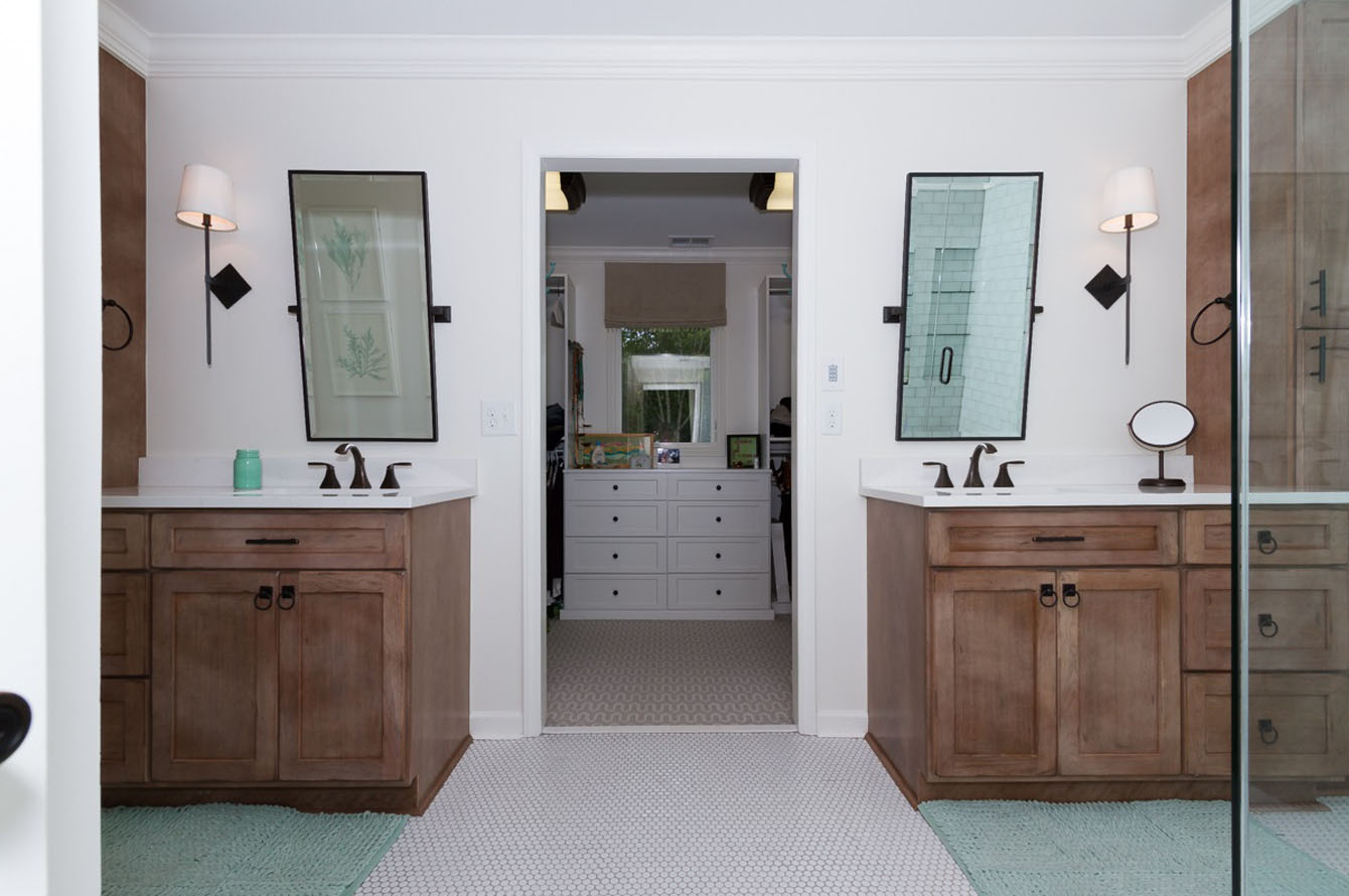 Modern bathroom remodeling with dual sinks, wooden cabinets, wall-mounted lamps, and a walk-in shower visible through a doorway.