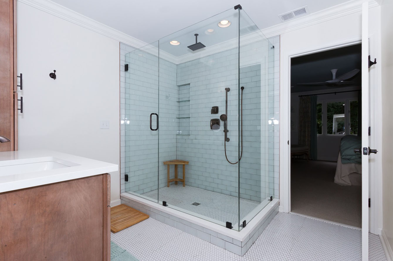 Modern bathroom remodeling featuring a large glass shower enclosure, pale blue tile walls, white flooring, a white bathtub, and a wooden stool.