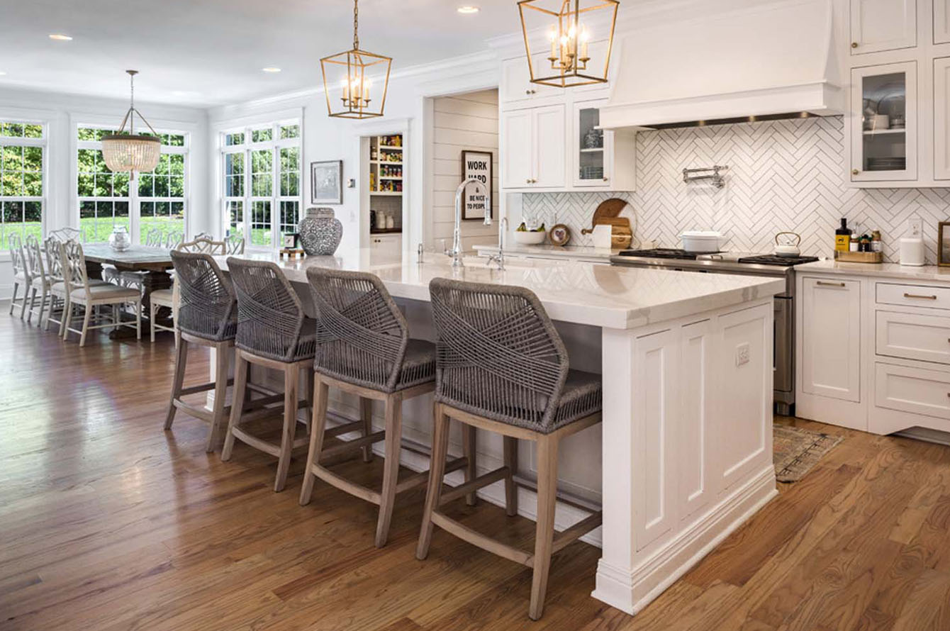 Elegant kitchen remodeling with white cabinetry, a central island with bar stools, and an adjacent dining area overlooking a garden.