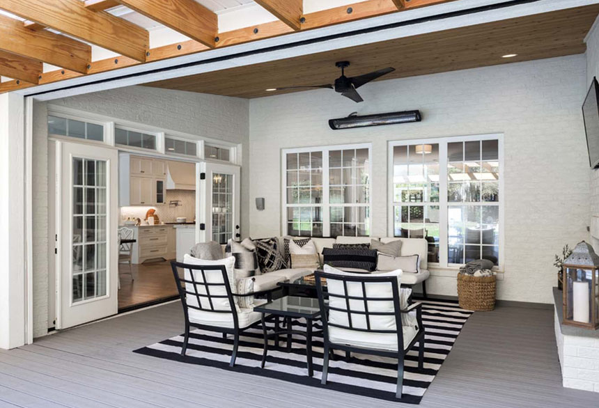 Modern indoor-outdoor sunroom with retractable glass doors, wood ceiling beams, and stylish furniture on a striped rug.