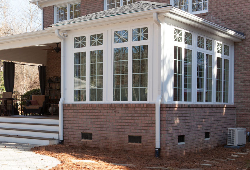 A brick house addition featuring large windows under a patio with a visible sunroom inside.