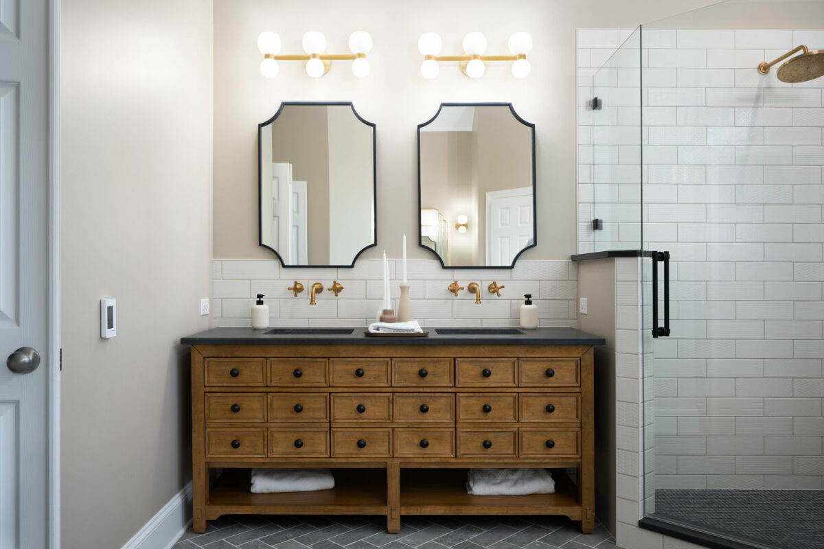 A bathroom with an apothecary-like vanity, double sink wall-mounted fixtures and two mirrors.