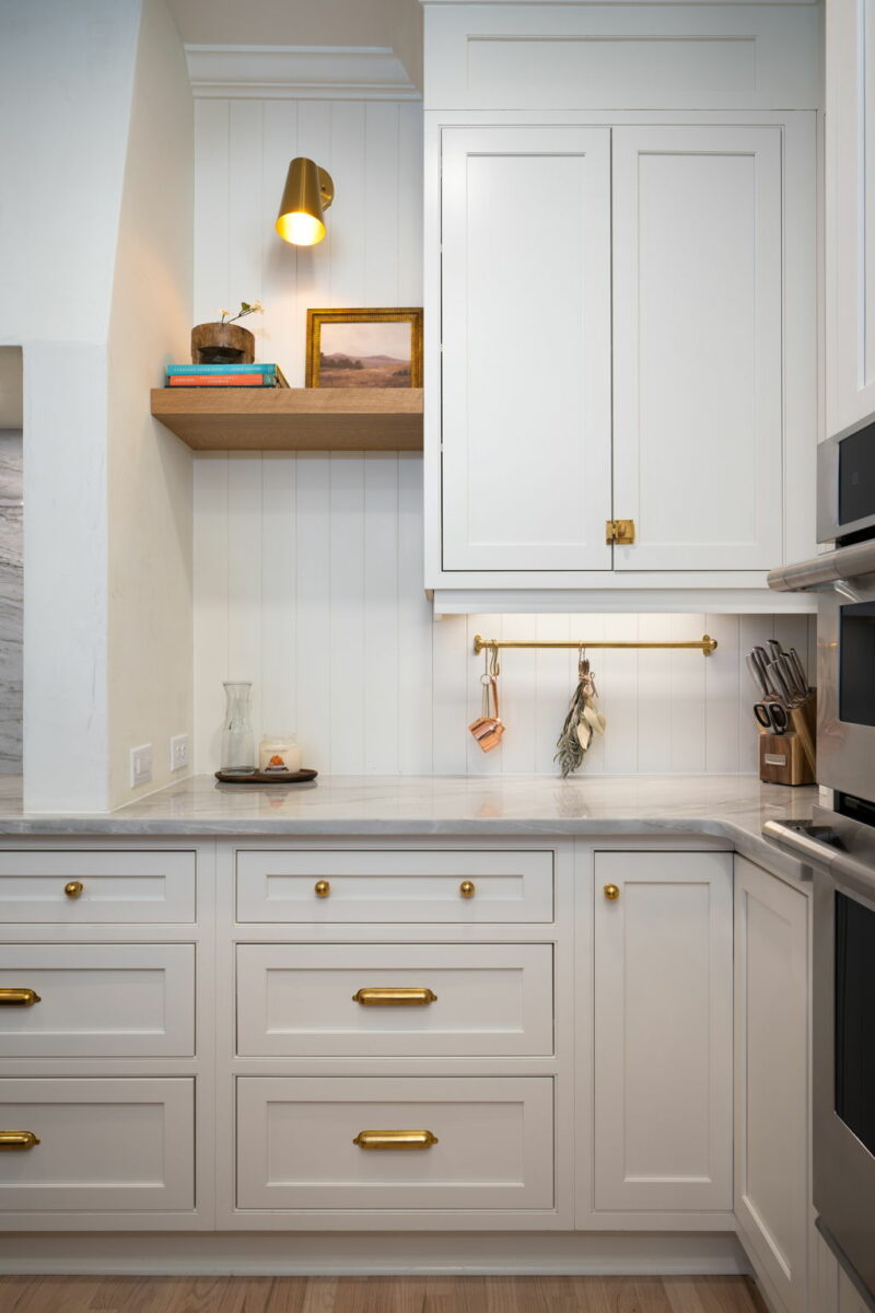 A kitchen with white cabinets, gold fixtures and an open decorative shelf.
