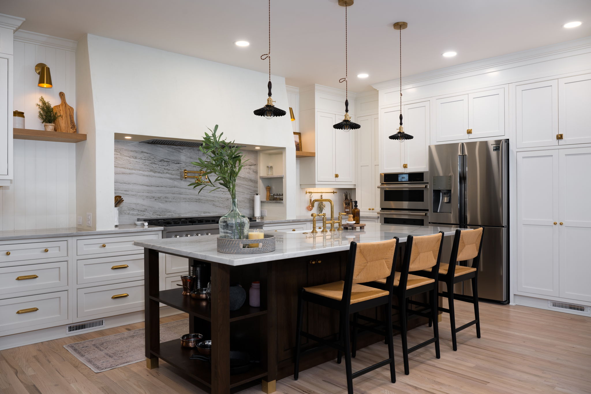 Modern kitchen with white cabinetry, marble backsplash, and a central kitchen island design with bar stools, complemented by pendant lighting and built-in appliances.