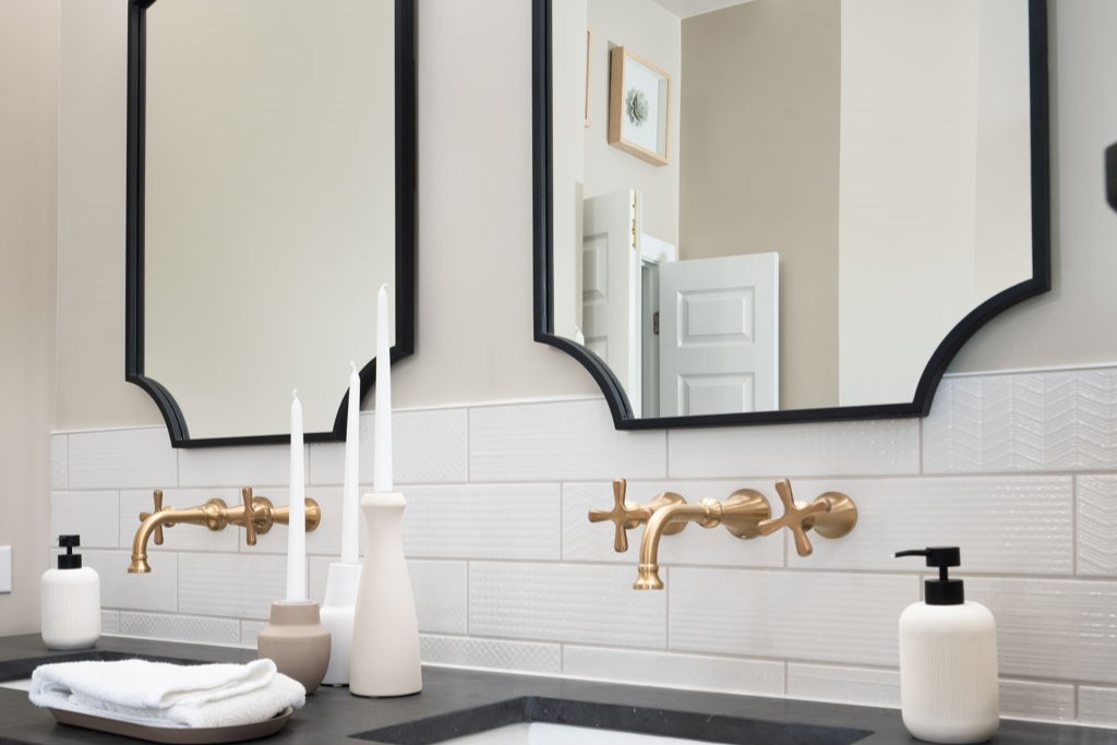 Master bathroom with two black-framed mirrors, brass faucets, and a white subway tile backsplash.