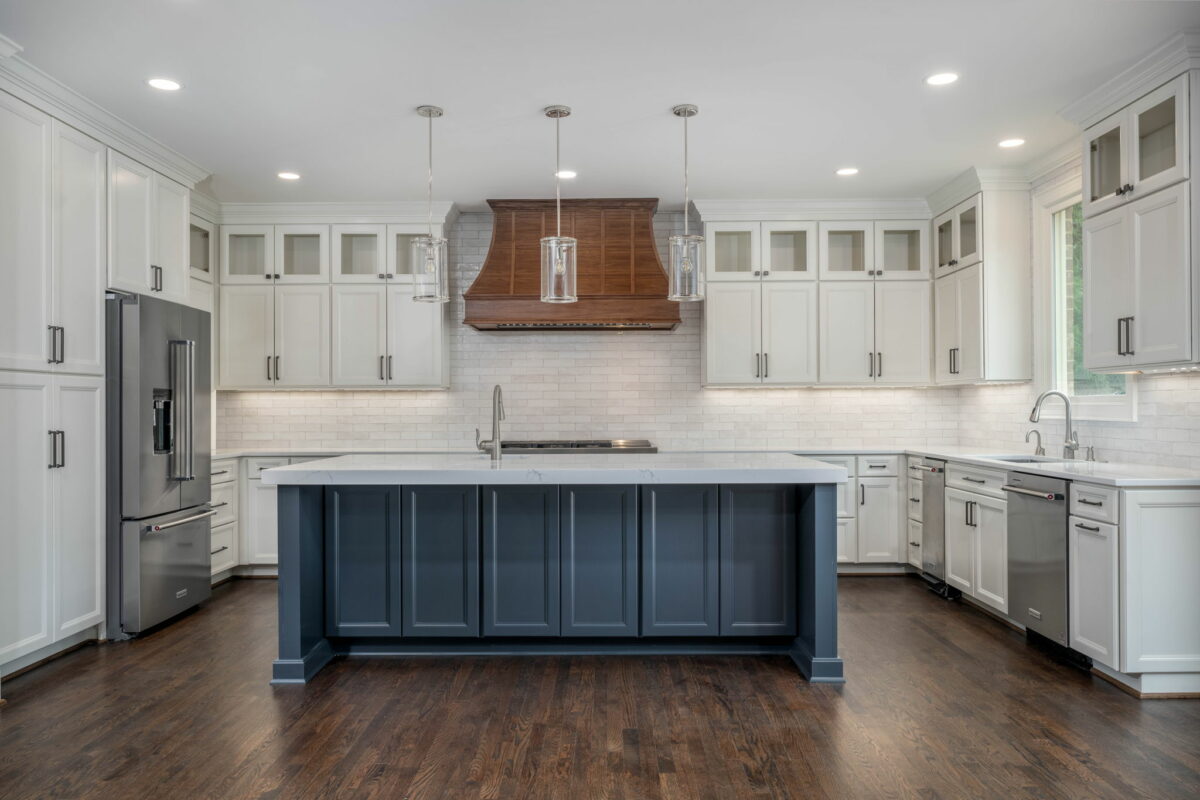 Modern kitchen interior, featuring white cabinetry, a blue island, stainless steel appliances, and hardwood floors.