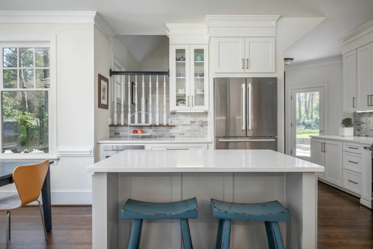 A modern Waxhaw kitchen with white cabinetry, stainless steel appliances, and a central island with two blue stools.