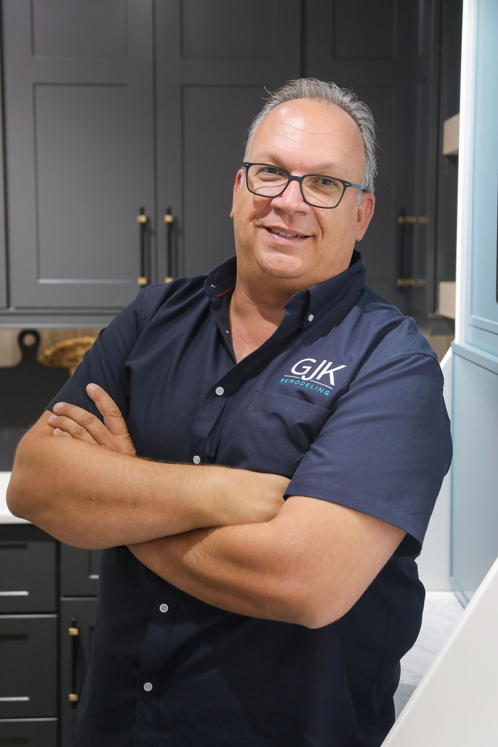 A man wearing glasses and a dark shirt with the logo "GIK" stands with arms crossed in a modern kitchen.