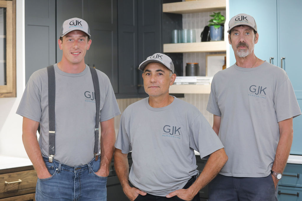 Three men wearing "GJK Remodeling" branded caps and shirts stand together in a kitchen setting, with cabinets and countertops visible in the background.