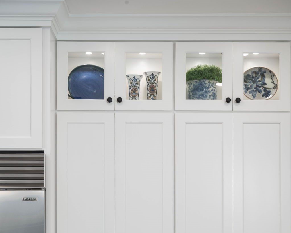 White kitchen cabinets with glass display sections show decorative bowls and pottery.