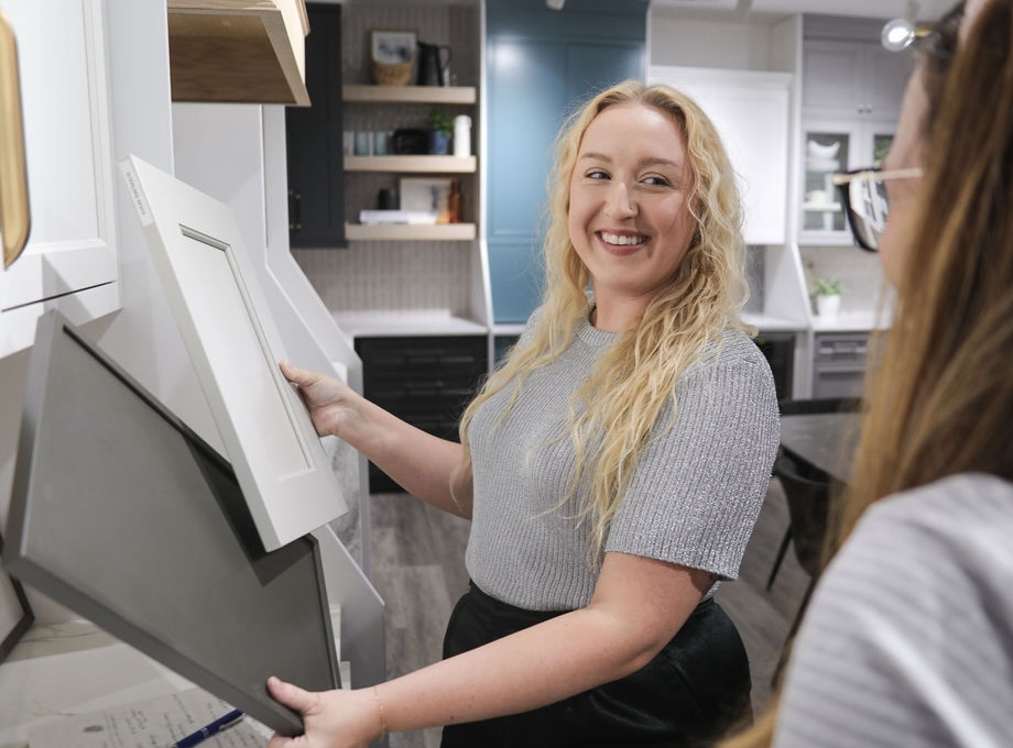 Our GJK Remodeling designer is smiling while holding sample cabinet doors in a showroom, conversing with another person.