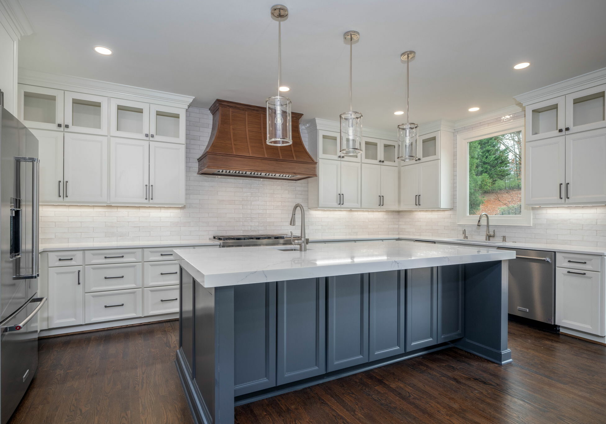 Modern kitchen with blue and white cabinetry, stainless steel appliances, pendant lights, and hardwood floors.