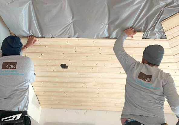 Two workers installing wooden panels on a ceiling, wearing matching jackets with a company logo, demonstrating how to finance a home renovation.